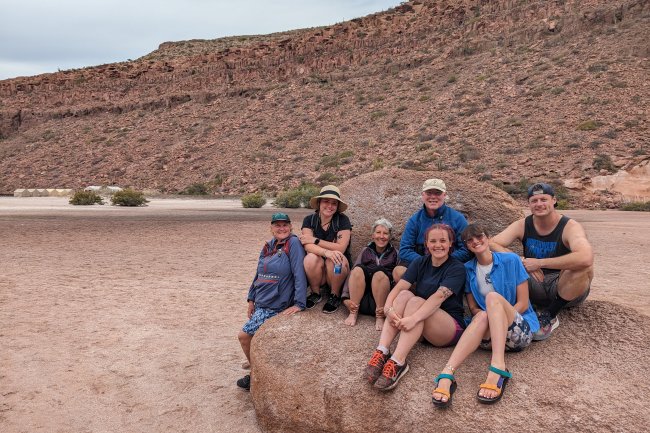 Part of the study group sits on a boulder in a desert landscape, smiling at the camera.