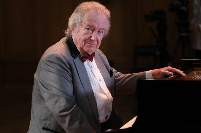Renowned pianist and Russian escapee Mikhail Voskresensky sits at a grand piano and turns toward the camera