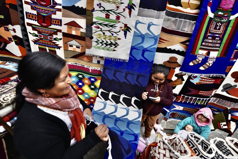 A vendor at the Otavalo market sells a variety of woven textiles.