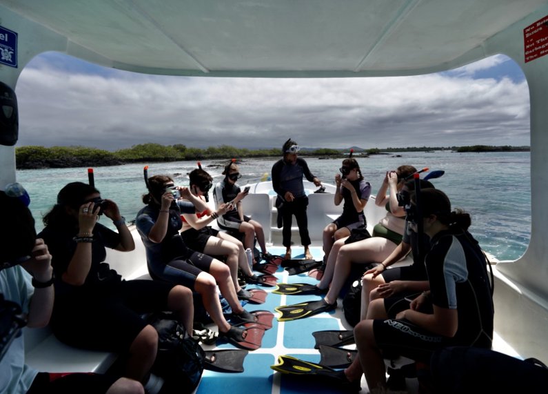 Students listen to an instructor as they sit on a boat before going snorkeling in the Galápagos.