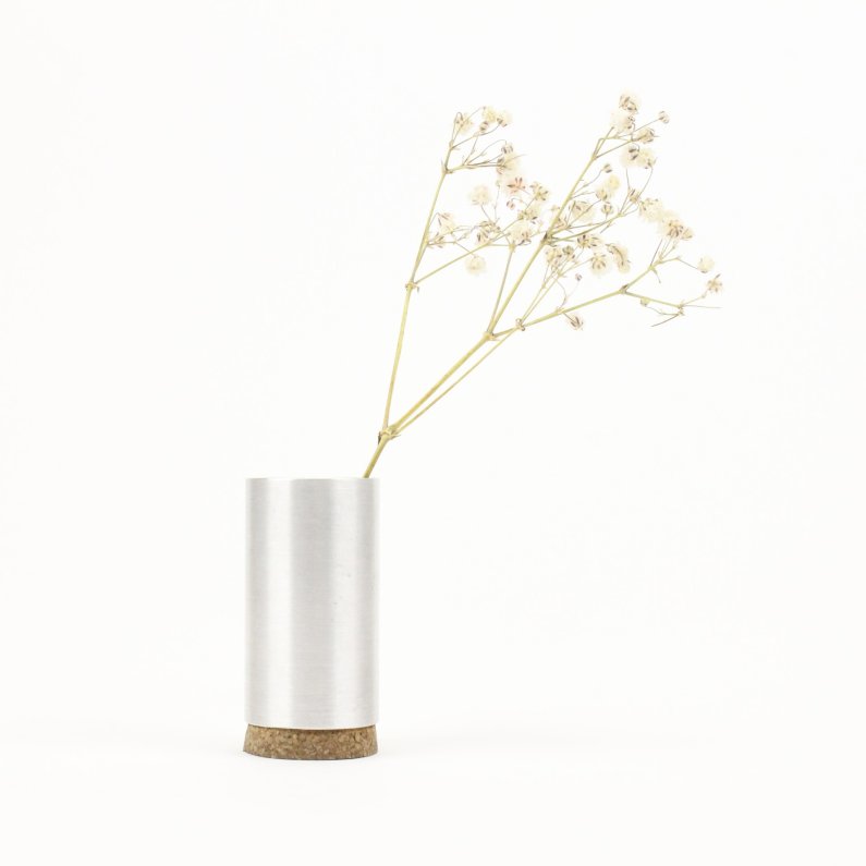  A small, silver-colored metal vase with a cork bottom holds a sprig of white baby's breath. The vase is placed on a white background, which makes the baby's breath appear to be floating in space. The image is simple and elegant, and the baby's breath adds a touch of whimsy.