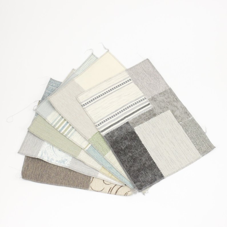 The image shows a stack of fabric swatches. The swatches are mostly blue and white, with some gray and brown. The patterns include solids, stripes, plaids, and florals. The swatches are arranged in a fan shape, with the largest swatch on the bottom and the smallest swatch on the top.