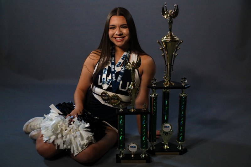 Amirah Casey wears her cheerleading uniform and sits next to a massive national championship trophy