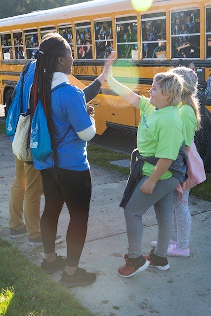 A fifth-grader gives a WWU student a high-five after getting off a yellow school bus. 