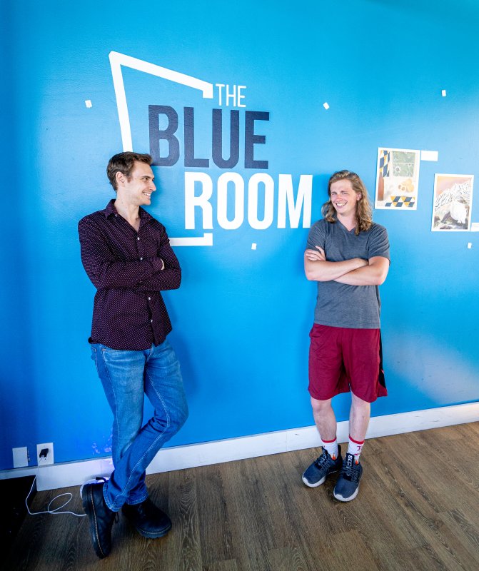 Ben Hodson and Martijn Wall lean against a wall painted with the logo from The Blue Room. 