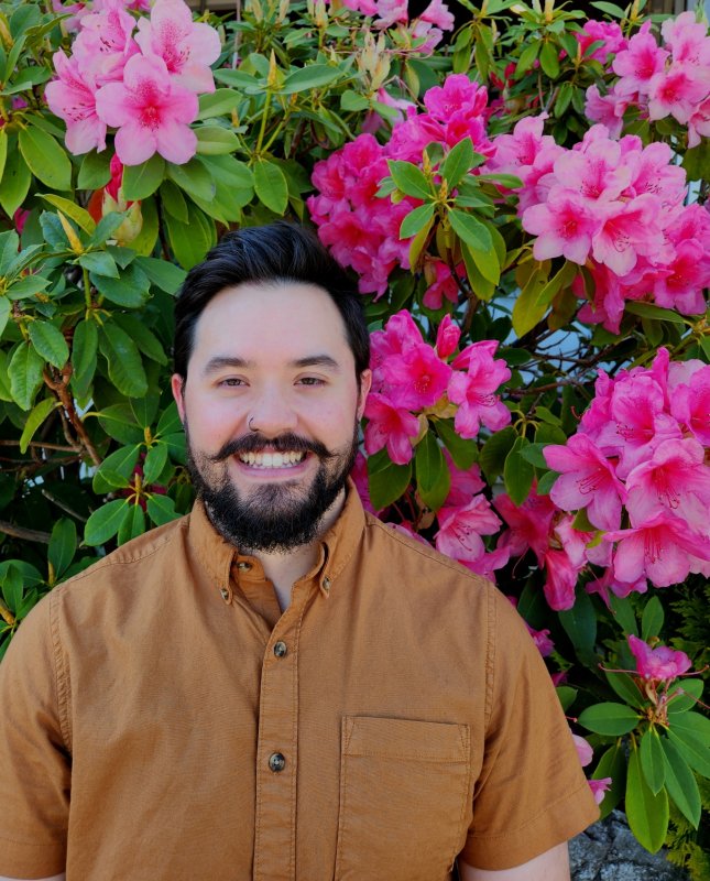 Dan Struble with a large bush of pink rhododendrons in the background