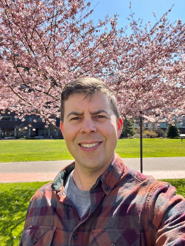 Michael Shepard takes a selfie on a sunny day on South Campus; behind him are cherry trees in bloom.