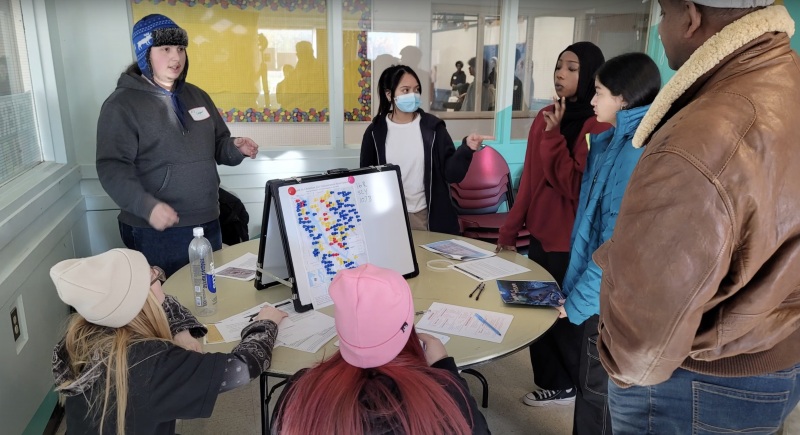 Screenshot of Environmental Justice Video phase 2 submission from Western, shows people gathered around a table discussing a graph
