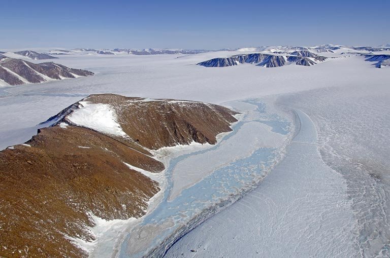 Aerial of the Greenland Ice Sheet, with mountaintops poking out of rivers of ice