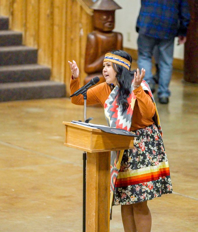 Santana Rabang gestures while speaking at a podium. 
