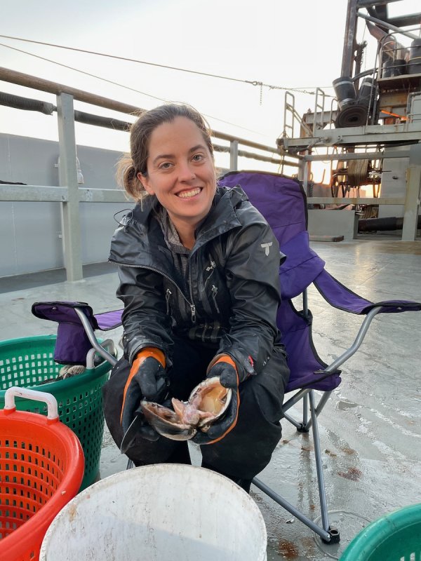 Nina on the deck of a research vessel, with a bucket of clams