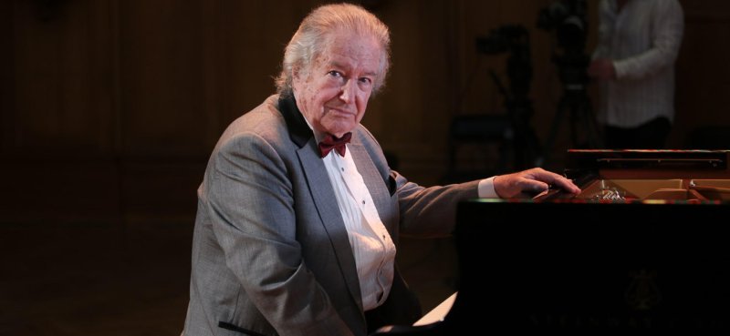 Renowned pianist and Russian escapee Mikhail Voskresensky sits at a grand piano and turns toward the camera
