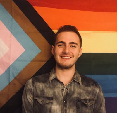 Andy Labay smiles in front of Pride Flag