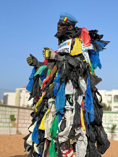 A man stands on a beach in Senegal, covered with so many plastic bags they look like the feathers of a bird.