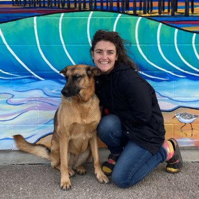 Elizabeth Baseman kneels with her dog in front of a mural.