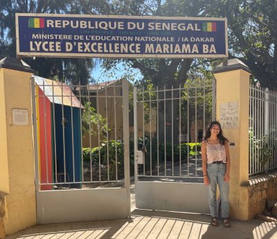 A student stands next to the entrance gate for a school in Senegal.