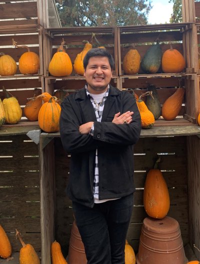 Miguel Gonzales Ramirez poses in front of a garden stand stacked with pumpkins and gourds