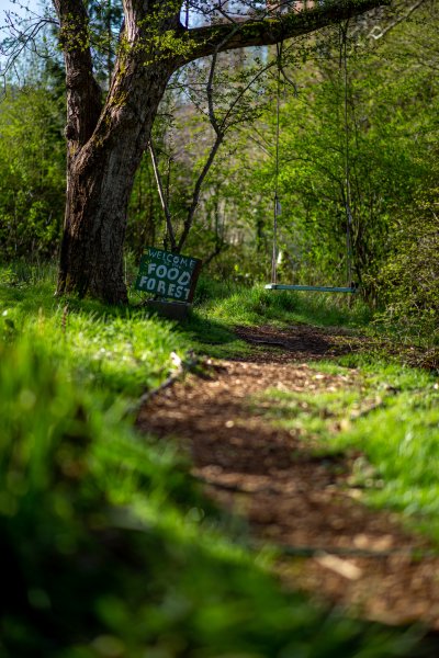 A sign between a tree and a trail welcomes visitors to the Outback Farm's Food Forest.