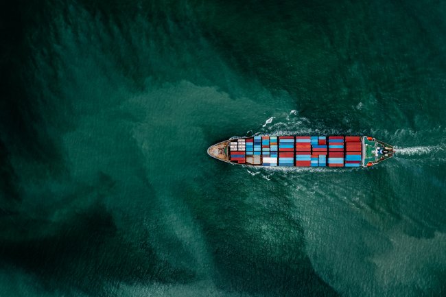 A freight ship photographed directly from above moves from right to left through deep sea green water
