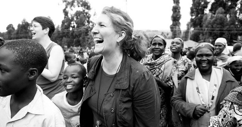 A black and white image of a white woman laughing with a group of African women and children.