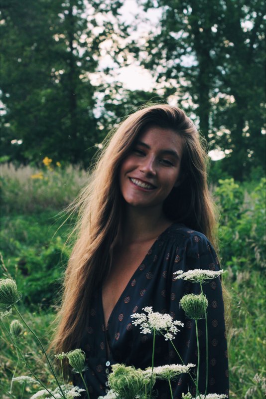 A young woman smiles in a field of wildflowers. The sun is shining brightly, and the flowers are in bloom.