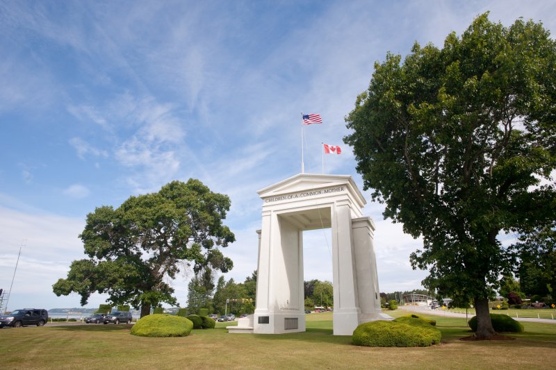 The US-Canada Peace Arch in Blaine, Washington, surrounded by large trees with Semiahmoo Bay visible in the background.