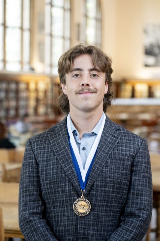 A young man in a suit and medal poses for a photo in a library.