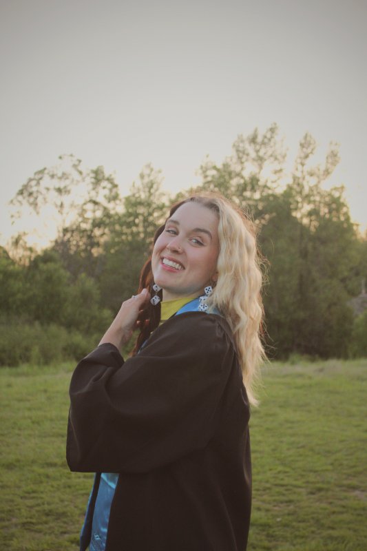 Bethany Lynch stands in a field, smiling, wearing a graduation gown