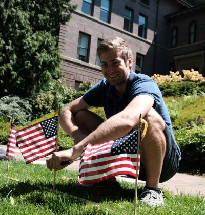 A student sits next to several flags that have been planted in Old Main lawn