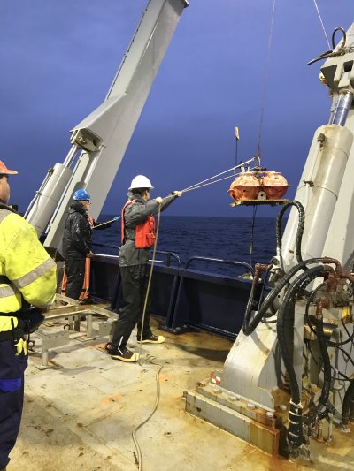 A student reaches out with a hook to grab a line as a crane pulls in a seismometer