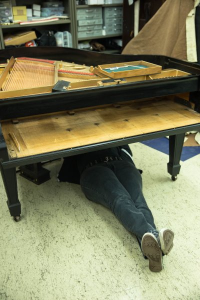 Only Michelle Stranges' feet and legs are visible as she works beneath a piano